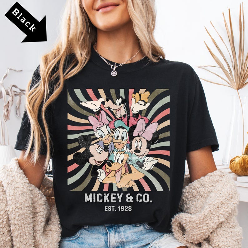 Puede incluir: Camiseta negra con un dise&ntilde;o gr&aacute;fico colorido de Mickey Mouse y sus amigos. El dise&ntilde;o incluye a Mickey, Minnie, Donald, Daisy, Goofy y Pluto, con el texto "MICKEY & CO. EST. 1928" en blanco.