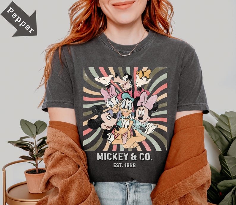 May include: Dark gray t-shirt featuring a colorful graphic of Mickey Mouse, Minnie Mouse, Donald Duck, Daisy Duck, Goofy, and Pluto. The shirt has the text "Mickey & Co. Est. 1928" in a vintage style.