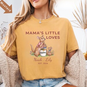 Puede incluir: Camiseta de color mostaza con el texto "MAMA'S LITTLE LOVES" y un gr&aacute;fico de familia de canguros. El gr&aacute;fico incluye un canguro, dos cr&iacute;as y un tarro de miel con la palabra "HAPPY". Personalizada con nombres y el a&ntilde;o 2026.