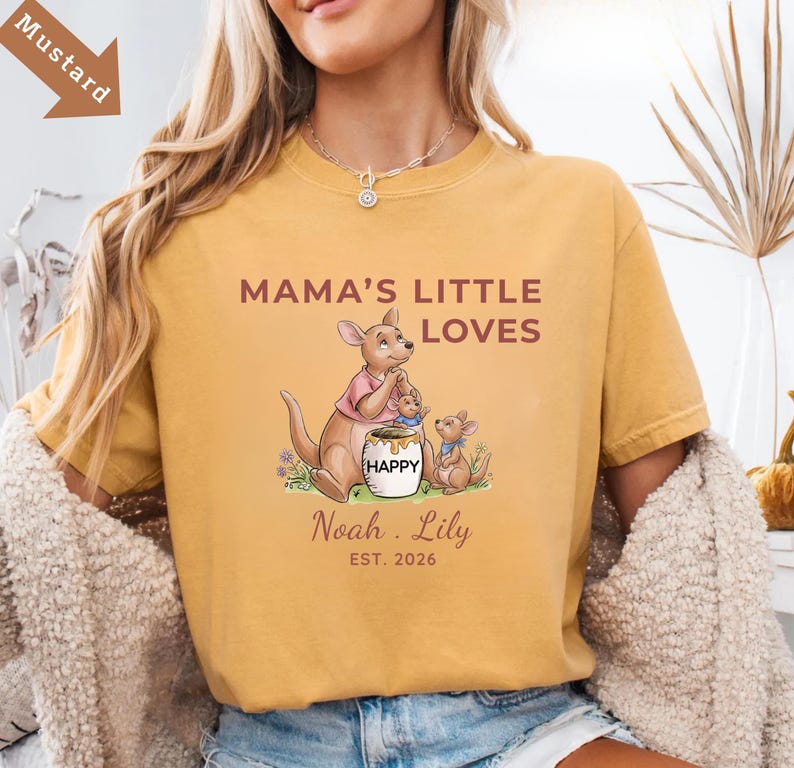Puede incluir: Camiseta de color mostaza con el texto "MAMA'S LITTLE LOVES" y un gr&aacute;fico de familia de canguros. El gr&aacute;fico incluye un canguro, dos cr&iacute;as y un tarro de miel con la palabra "HAPPY". Personalizada con nombres y el a&ntilde;o 2026.