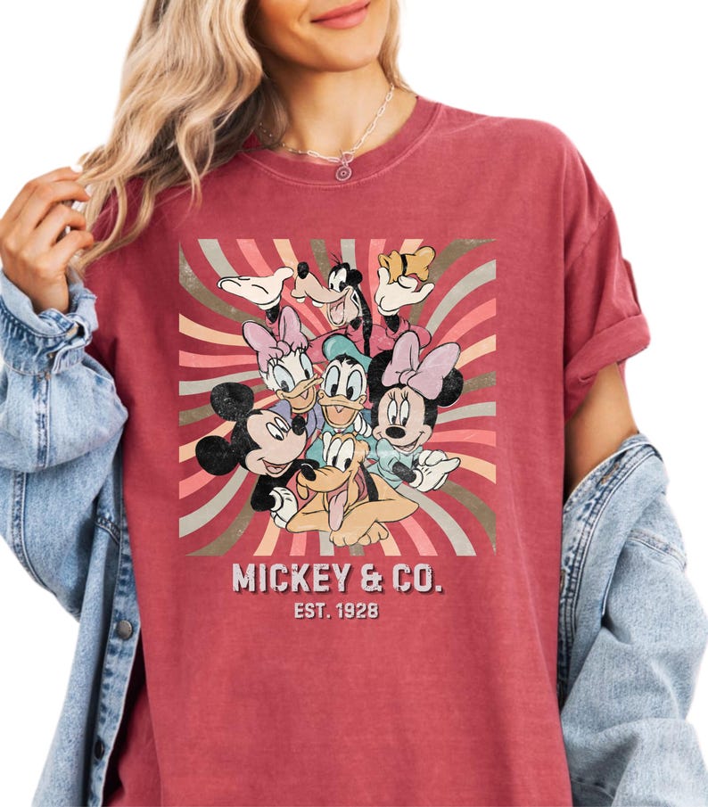 Puede incluir: Camiseta roja con un gr&aacute;fico de Mickey Mouse, Minnie Mouse, Donald Duck, Daisy Duck, Goofy y Pluto. El dise&ntilde;o est&aacute; sobre un fondo de rayas retro. El texto "MICKEY & CO. EST. 1928" est&aacute; impreso debajo de los personajes.