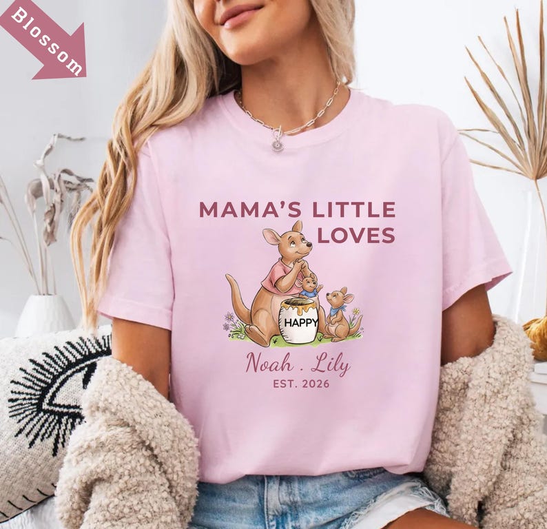 Puede incluir: Camiseta rosa claro con el texto "MAMA'S LITTLE LOVES" y un gr&aacute;fico de familia de canguros. El gr&aacute;fico incluye un canguro, dos cr&iacute;as y un tarro de miel. Debajo del gr&aacute;fico est&aacute;n los nombres "Noah . Lily" y el a&ntilde;o "EST. 2026".