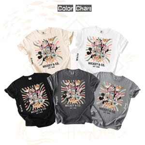 Puede incluir: Una carta de colores muestra cinco camisetas en marfil, blanco, negro, pimienta y gris. Cada camiseta presenta un gr&aacute;fico de Mickey Mouse y sus amigos con el texto "MICKEY & CO. EST. 1928" en un dise&ntilde;o retro.