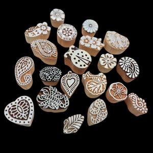 May include: A collection of wooden block stamps with various designs, including floral patterns, paisley, and a ladybug. The stamps are made of light-colored wood with white designs, perfect for textile printing or crafting.