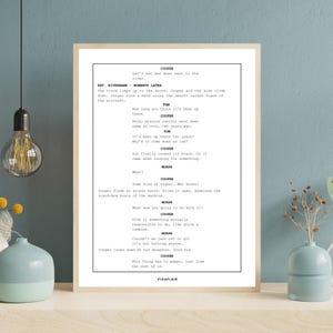 May include: A framed print featuring a movie script with the title "COOPER" at the top. The script is in black text on a white background. The print is in a light wood frame and is displayed on a blue wall.