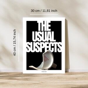 May include: A framed art print, 30 cm wide and 40 cm tall, displays the text "THE USUAL SUSPECTS" in large white letters against a black background. A broken white porcelain object is at the bottom. The print is on a wooden floor.