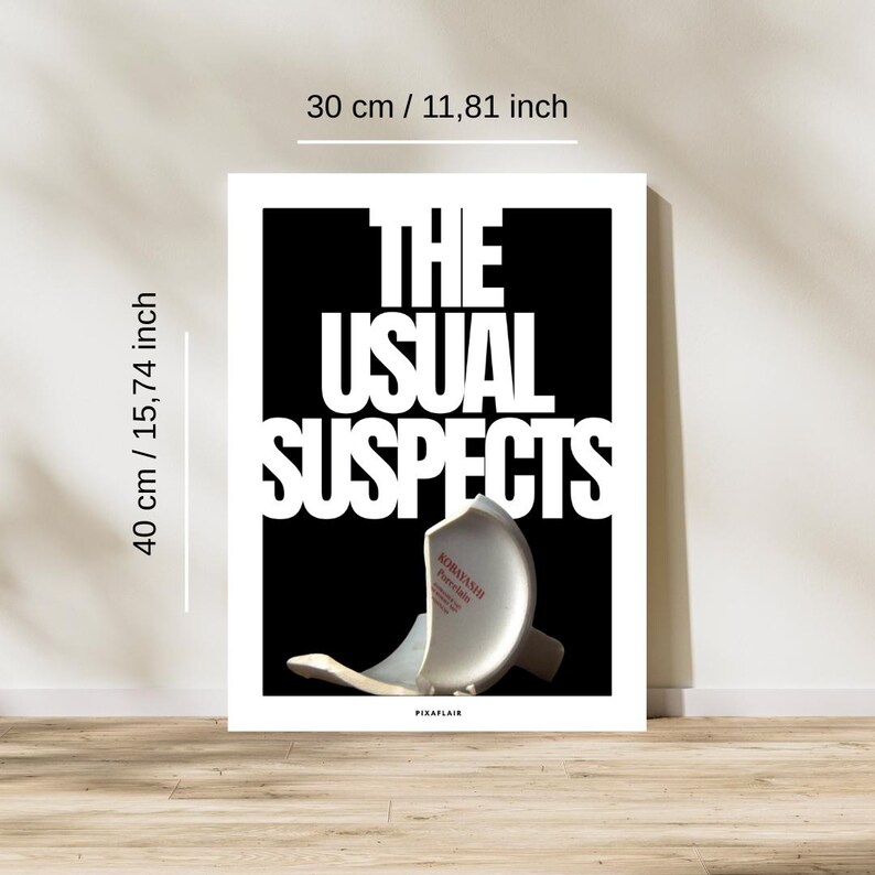 May include: A framed art print, 30 cm wide and 40 cm tall, displays the text "THE USUAL SUSPECTS" in large white letters against a black background. A broken white porcelain object is at the bottom. The print is on a wooden floor.