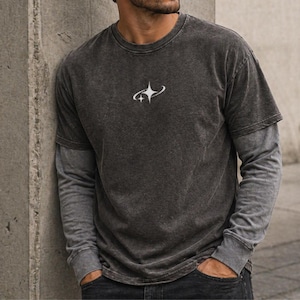 May include: Dark gray t-shirt with a white graphic of two curved lines and a starburst design. The shirt has a layered look with a long-sleeved gray undershirt. The shirt is made of a soft, comfortable material.
