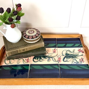 May include: Wooden serving tray with a tiled surface featuring a floral design in pink, green, and blue. The tray holds a white pitcher with berries, a decorative box, and two vintage books.