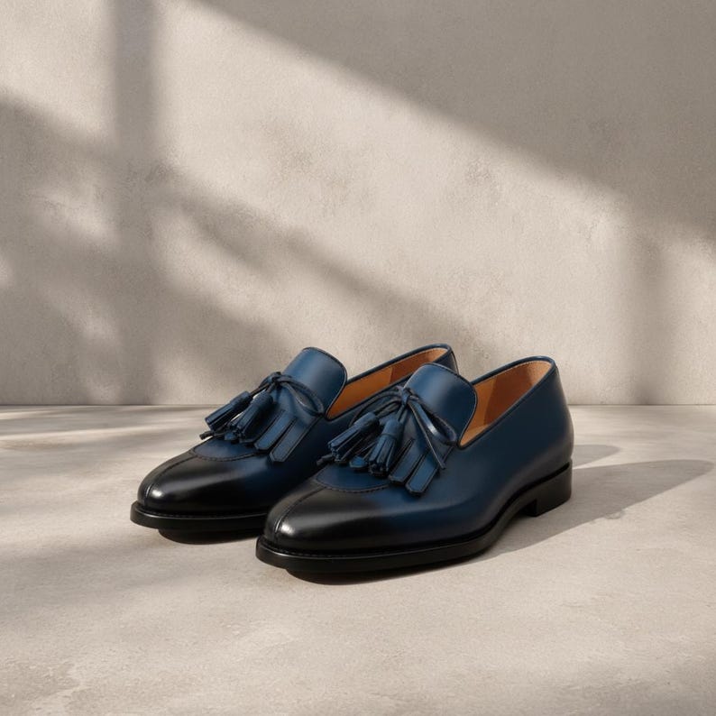 Handmade men's navy blue patina tassel loafers in genuine cowhide leather with hand-burnished indigo-to-midnight colour graduation and tonal hand-cut leather tassel, photographed at low angle on a concrete surface with cedar shoe trees — bespoke burnished slip-on formal dress loafers.