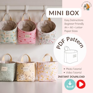 May include: Several fabric mini boxes with floral and patterned designs, featuring beige handles and lining. The boxes are suspended from a white rail. The image includes text that says "MINI BOX" and "PDF Pattern".