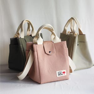 Small tote bag in olive green and blush pink canvas, featuring a snap button closure and "Lunch" label.