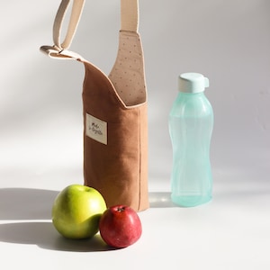 Detailed view of the adjustable webbing strap and metal hardware on a handmade bottle carrier.