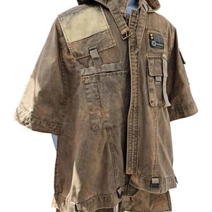 May include: Brown short-sleeved jacket with multiple pockets, straps, and a hood. The jacket has a distressed appearance with a patch on the shoulder and a small emblem on the chest. The garment is displayed on a mannequin.