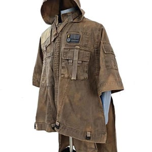 May include: Brown hooded jacket with multiple pockets and a unique design. The jacket features a patch with a rectangular design. The garment has a distinctive, weathered appearance and a short-sleeved design.