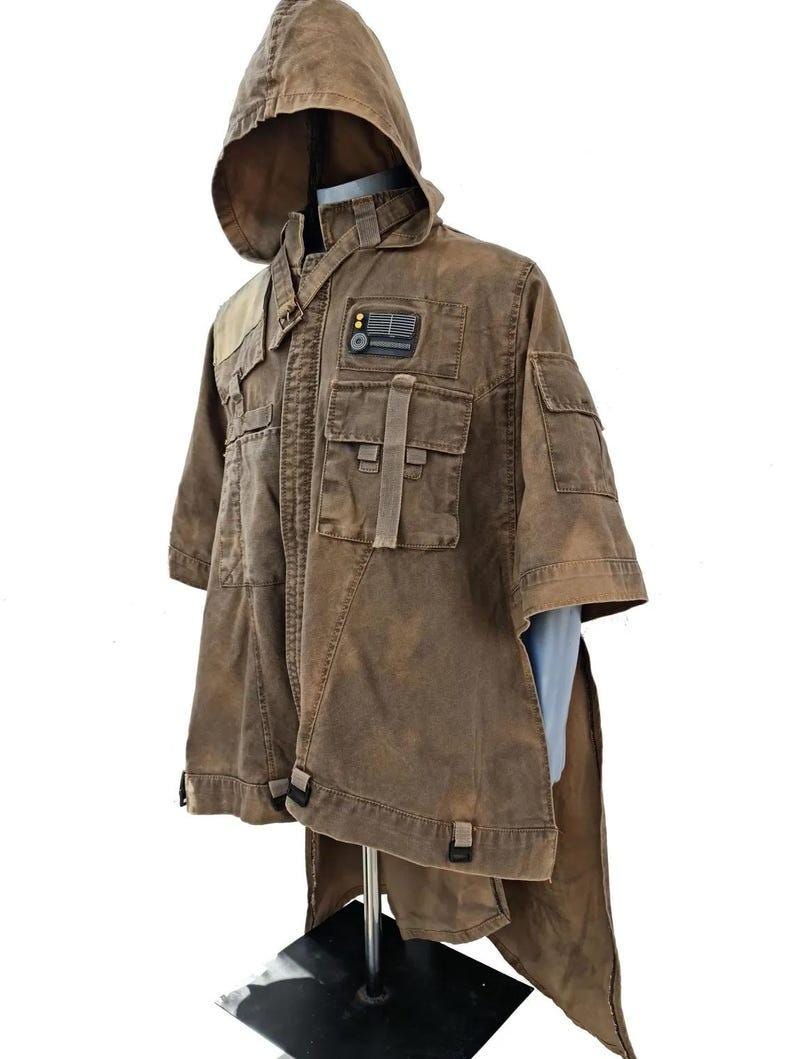 May include: Brown hooded jacket with multiple pockets and a unique design. The jacket features a patch with a rectangular design. The garment has a distinctive, weathered appearance and a short-sleeved design.