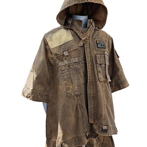 May include: Brown hooded jacket with multiple pockets and straps. The jacket has a unique design with a weathered appearance, featuring a hood and short sleeves. The jacket is displayed on a mannequin, showcasing its details and construction.