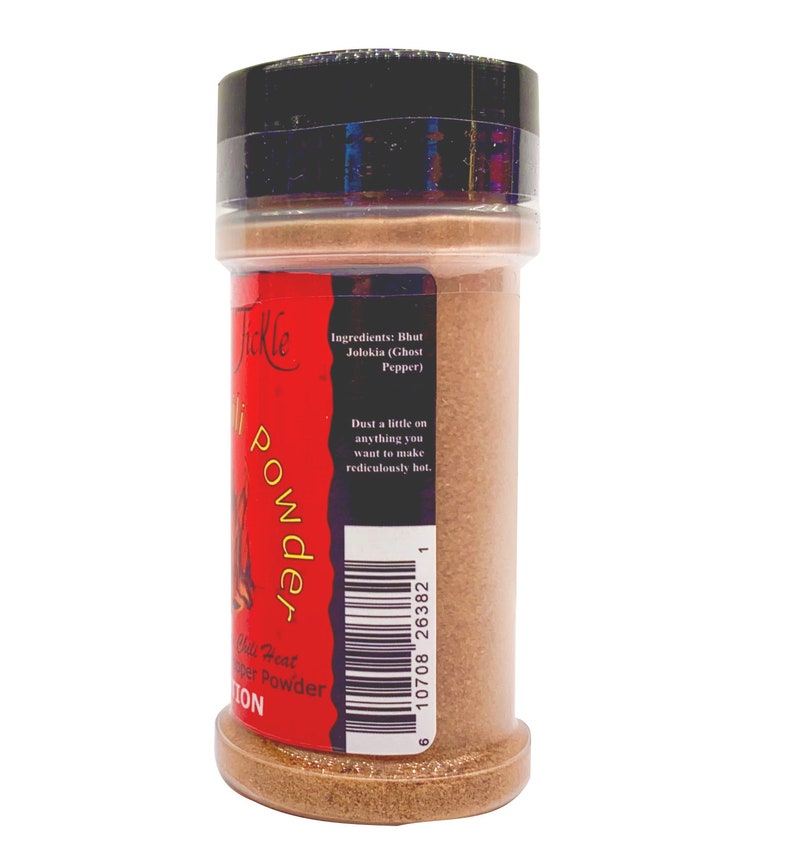 Puede incluir: Un tarro de especias rojo y negro con una etiqueta que dice "Chili Heat Pepper Powder" y "Tickle" con un gr&aacute;fico de llama. La etiqueta tambi&eacute;n enumera los ingredientes como "Bhut Jolokia (Ghost Pepper)" y dice "Espolvorea un poco en cualquier cosa que quieras hacer rid&iacute;culamente picante." El c&oacute;digo de barras es 10708 26382 1.