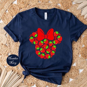 A navy blue t-shirt with a red bow and a design of red strawberries on it, placed on a woven mat.