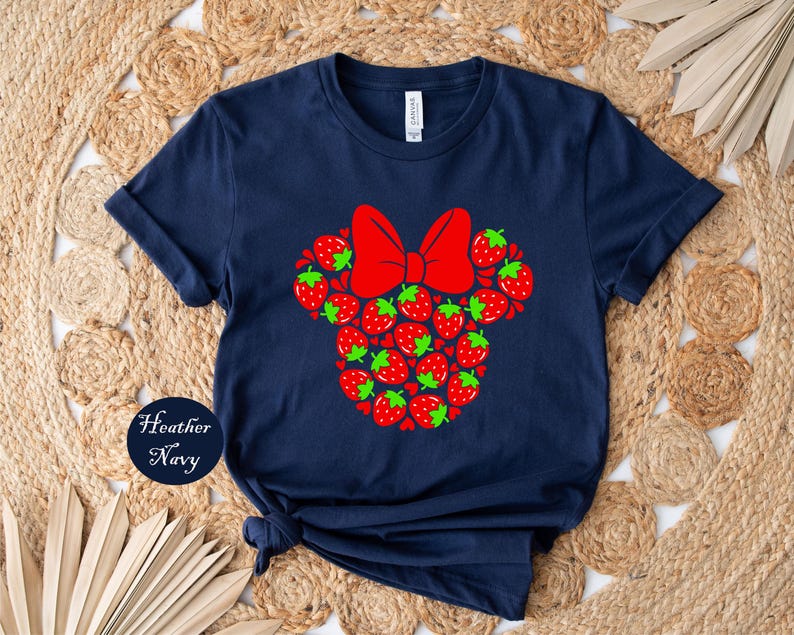 A navy blue t-shirt with a red bow and a design of red strawberries on it, placed on a woven mat.