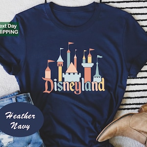 a navy blue t-shirt with a graphic of a castle and the word "Disneyland" printed on it, along with a pair of jeans and a brown boot.