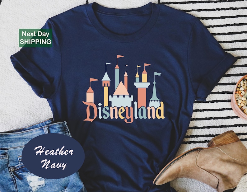 a navy blue t-shirt with a graphic of a castle and the word "Disneyland" printed on it, along with a pair of jeans and a brown boot.