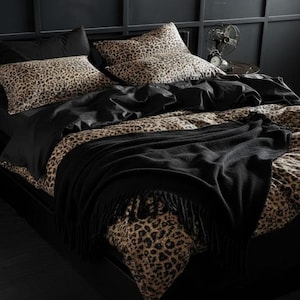 Könnte beinhalten: Ein Bett mit Leopardenmuster-Bettwäsche, einschließlich Kissenbezügen und einem Bettbezug. Eine schwarze Decke mit Fransen ist über dem Fußende des Bettes drapiert. Der Raum hat schwarze Wände und Möbel.