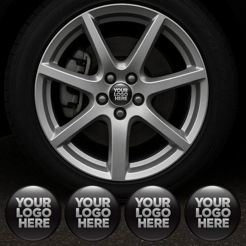 May include: A silver alloy car wheel with a black tire. The wheel has a star-like design with five spokes. The center cap displays the text "YOUR LOGO HERE" in white on a black background. Four additional caps are below.