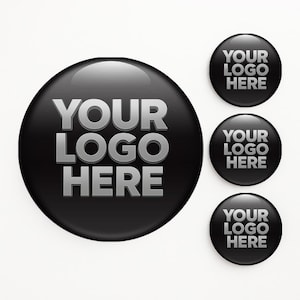 May include: Black glossy round buttons with the text "YOUR LOGO HERE" in silver. The image shows a large button and three smaller buttons, all with the same design. The buttons have a reflective surface.