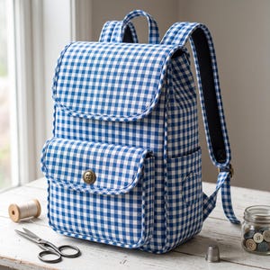 Peut inclure: Un sac &agrave; dos &agrave; motif vichy bleu et blanc dot&eacute; d'un rabat sup&eacute;rieur, d'une poche avant ferm&eacute;e par un bouton m&eacute;tallique unique et de bretelles r&eacute;glables. Le sac &agrave; dos pr&eacute;sente une forme rectangulaire structur&eacute;e avec des bords passepoil&eacute;s.