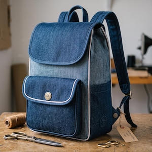 Peut inclure: Un sac &agrave; dos en jean bleu dot&eacute; d'un rabat sup&eacute;rieur, d'une poche avant ferm&eacute;e par un bouton unique et de bretelles r&eacute;glables. Le sac est rehauss&eacute; d'un passepoil de couleur claire sur les bords et comporte un petit logo circulaire sur le c&ocirc;t&eacute;.