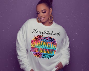 May include: A white sweatshirt with the text "She is clothed with STRENGTH AND DIGNITY" in black and rainbow colors. The graphic has a leopard print design. The sweatshirt is a casual style.