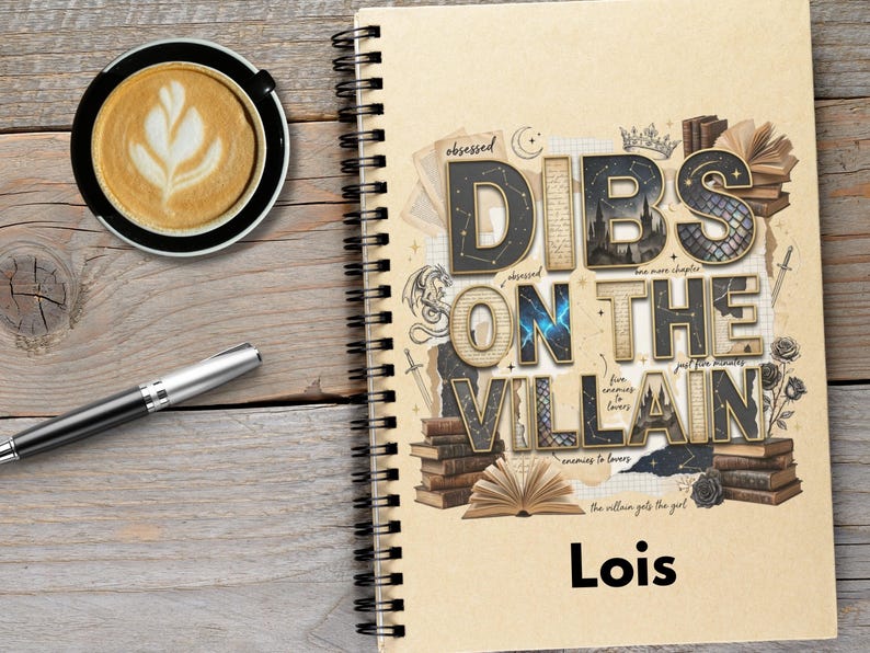 May include: A spiral-bound notebook with the text "DIBS ON THE VILLAIN" in a decorative font, with the name "Lois" below. A cup of coffee with latte art and a pen are on a wooden surface.