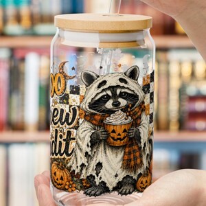May include: A clear glass tumbler with a bamboo lid and a glass straw. The glass features a graphic of a raccoon wearing a ghost costume, holding a pumpkin mug with whipped cream, surrounded by pumpkins and the text "BOO CREW".