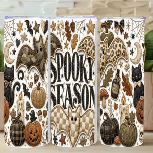 May include: A cylindrical tumbler featuring a repeating pattern of Halloween-themed icons including black cats, bats with various textures, pumpkins, candles, and autumn leaves. The text SPOOKY SEASON is printed in large black letters in the center.
