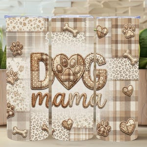 May include: A beige tumbler with a patchwork design featuring paw prints, hearts, and bone shapes. The words "DOG mama" are prominently displayed. The tumbler is surrounded by plants in beige pots.