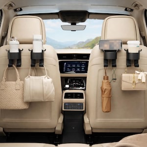 Puede incluir: Organizadores de asiento de coche negros con un diseño caprichoso, que sostienen una botella de agua, una taza de café, un teléfono y pequeños bolsos. Los organizadores están sujetos a los reposacabezas, con un paraguas marrón.