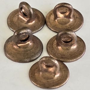 May include: Five antique copper-colored buttons with a loop on the top. The buttons are round and have a slightly domed shape. The buttons are arranged in a circular pattern.
