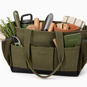 May include: An olive green garden tote bag filled with gardening tools, gloves, and rosemary sprigs. The bag has multiple pockets and a black base. The word "James" is embroidered on the front.