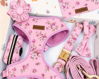 May include: A pink pet accessory set featuring a floral pattern, including a harness with a DDPAWS label, a leash, a collar with a gold buckle engraved with the name Daisy, a bow tie, a flower attachment, and a waste bag dispenser.