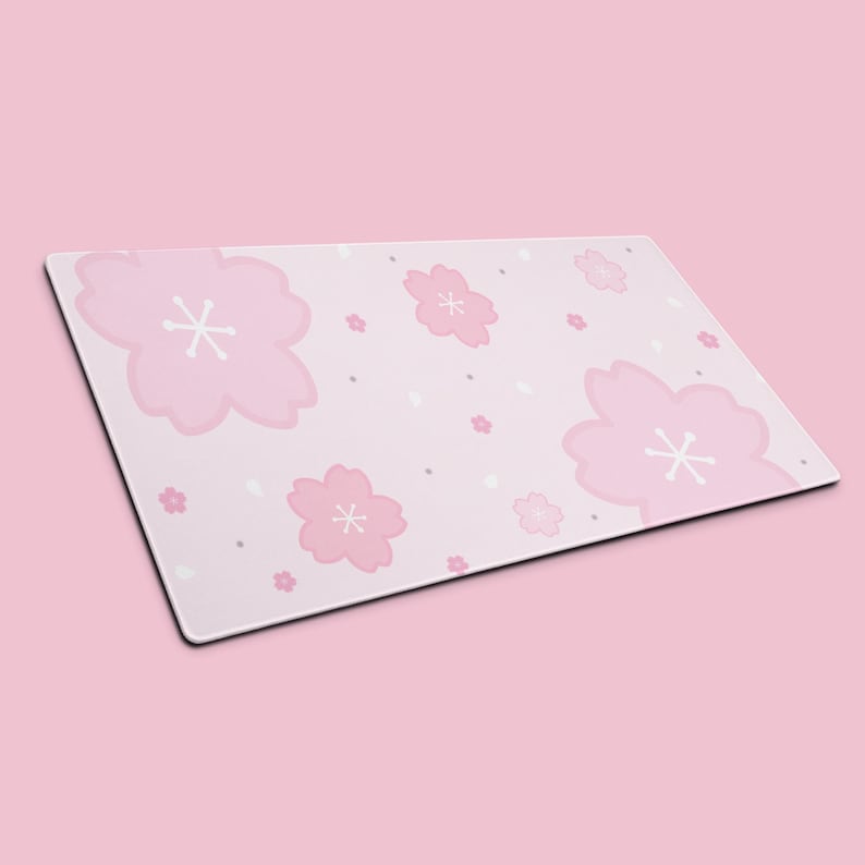 K&ouml;nnte beinhalten: Rechteckige, rosa Schreibtischunterlage mit einem sich wiederholenden Muster aus stilisierten rosa Kirschbl&uuml;ten mit wei&szlig;en Zentren. Kleine wei&szlig;e und graue Punkte sind &uuml;ber dem hellrosa Hintergrund verstreut. Die Matte hat einen schwarzen Rand.