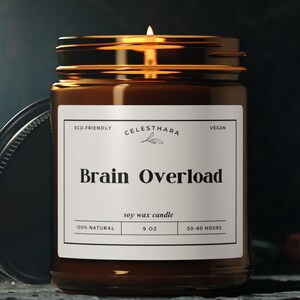 Könnte beinhalten: Eine brennende Sojawachskerze in einem braunen Glas mit schwarzem Deckel. Auf dem Etikett steht "Brain Overload" und "9 oz". Die Kerze ist umweltfreundlich und vegan. Die Kerze steht auf einer dunklen Oberfläche.