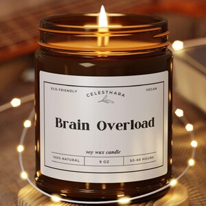 May include: A lit soy wax candle in a brown glass jar with the text "Brain Overload" on a white label. The candle sits on a wooden coaster, surrounded by string lights. The candle is 9 oz and burns for 30-40 hours.