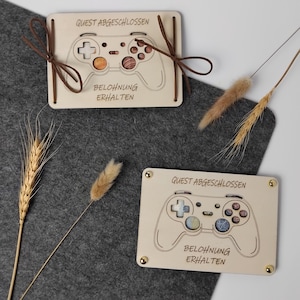 Könnte beinhalten: Zwei rechteckige, helle Holzschilder mit der eingravierten Umrisszeichnung eines Gamecontrollers. Auf jedem Schild steht der Text "QUEST ABGESCHLOSSEN" und "BELOHNUNG ERHALTEN". Ein Schild hat braune Kordeln, das andere vier goldfarbene Metallnieten.
