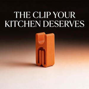 Puede incluir: Un clip de cocina naranja con un diseño único, con el texto "THE CLIP YOUR KITCHEN DESERVES". El clip tiene una serie de líneas verticales y una base curva. El fondo es un degradado de negro y blanco.