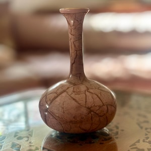 Könnte beinhalten: Eine dekorative Vase mit rundem Boden und schlankem Hals. Die Vase hat ein rissiges, strukturiertes Muster in Braun- und Rosatönen. Der Rand der Vase ist hellrosa.