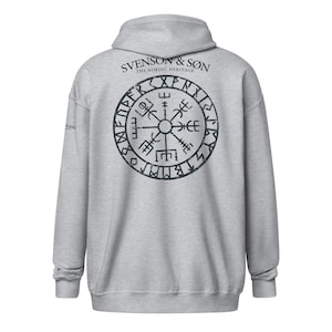 Może przedstawiać: Szara bluza z kapturem z dużym, czarnym, zniszczonym nadrukiem na plecach. Grafika to okrągły kompas wikingów z napisem "SVENSON & SON THE NORDIC HERITAGE" powyżej. Bluza ma kaptur i długie rękawy.