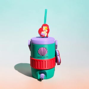 May include: A teal water cooler with a purple lid and red accents. The cooler features a seashell logo and the text "ARIEL & CO." A red-haired mermaid figure adorns the top, and a teal straw extends from the lid.