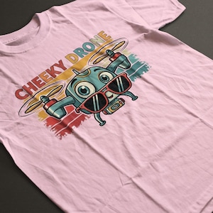 Könnte beinhalten: Hellrosa T-Shirt mit einem Cartoon-Drohnen-Charakter, der eine Sonnenbrille trägt. Der Text "CHEEKY DRONE" ist in einem farbenfrohen Retro-Stil über der Drohne aufgedruckt. Das Shirt besteht aus weichem Material.