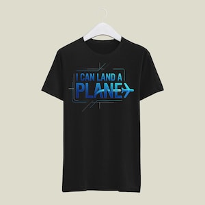 May include: Black t-shirt with the text "I CAN LAND A PLANE" in blue and white. A blue airplane graphic is on the right side of the text. The shirt is hanging on a white hanger.